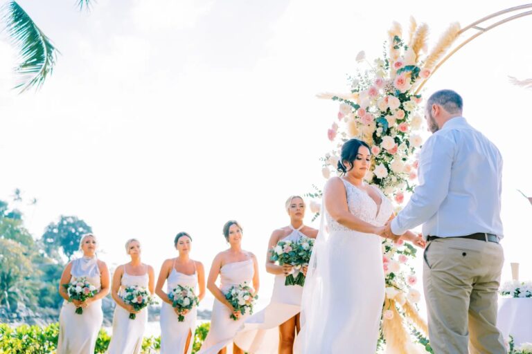 A bride and groom exchange rings under a pampas grass and rose arch, with bridesmaids in white behind, at Katathani Phuket, Phuket Romance