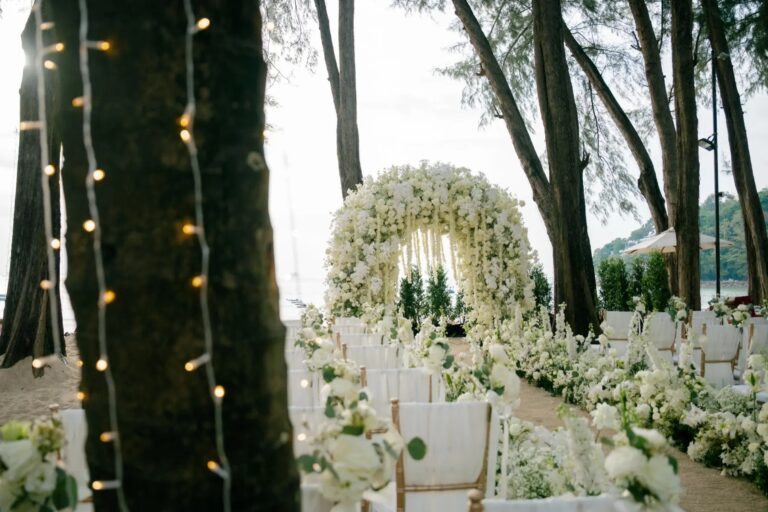 Rows of white chairs and a flower-lined aisle leading to a white floral arch beneath casuarina trees hung with fairy lights, Phuket Romance
