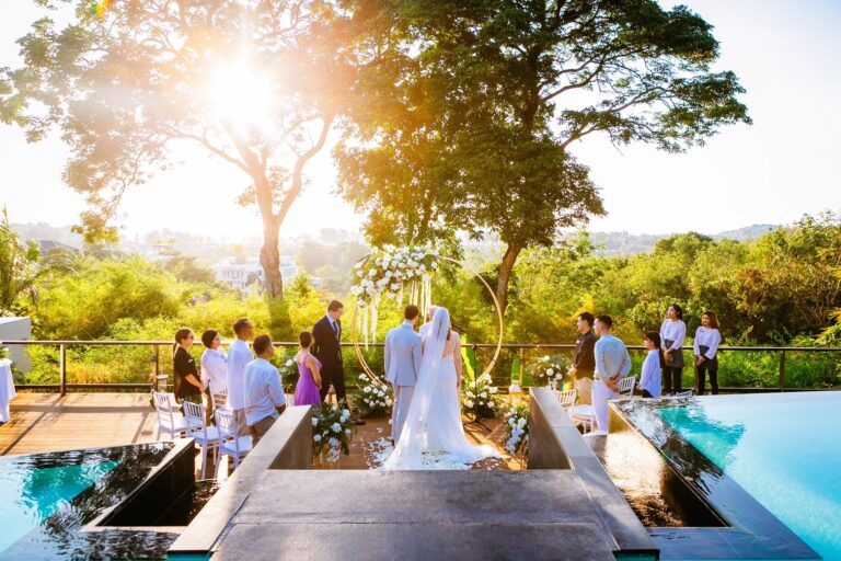 A couple at a floral arch on a deck beside an infinity pool, with hills and low sun behind, at The Pavilions Phuket, Phuket Romance