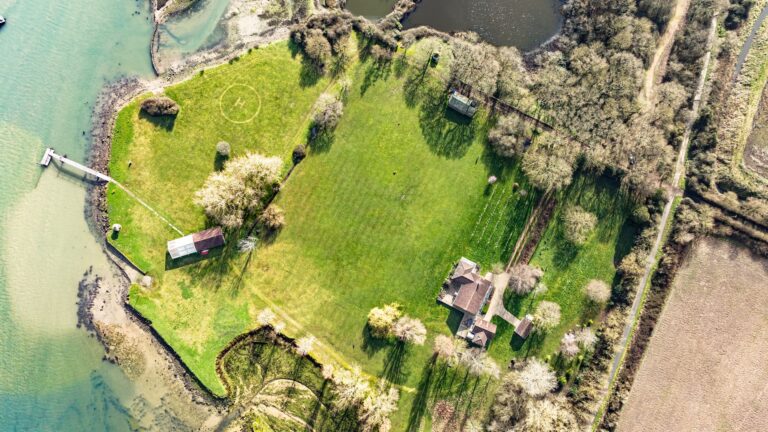 Looking straight down on the estate: the house among trees, the lawn with its marked helicopter landing circle, the boathouse and the jetty into the river, Pinkmead Estate