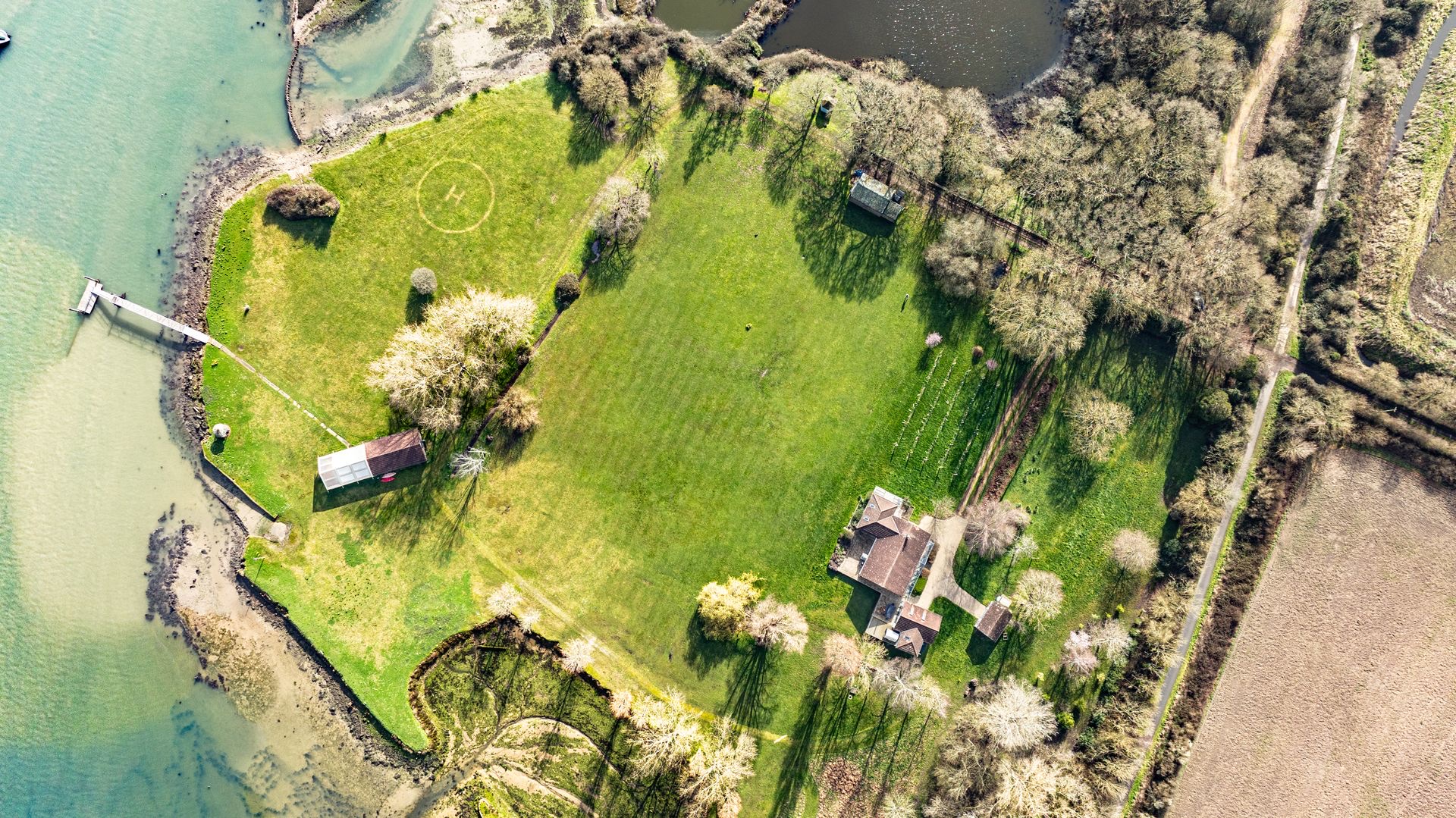 Looking straight down on the estate: the house among trees, the lawn with its marked helicopter landing circle, the boathouse and the jetty into the river, Pinkmead Estate