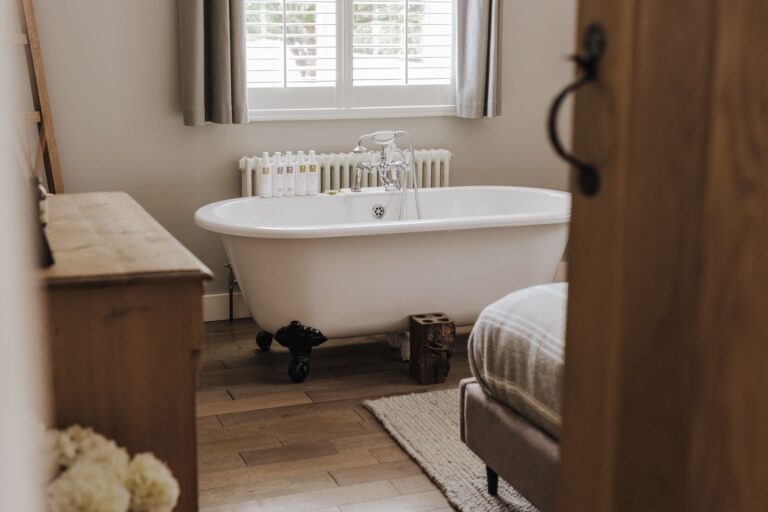 A bedroom with a roll-top bath on claw feet beneath the window, seen through an oak plank door, Pinkmead Estate