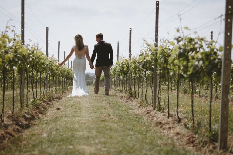 A couple walking hand in hand away down a grass path between the vines, Pinkmead Estate
