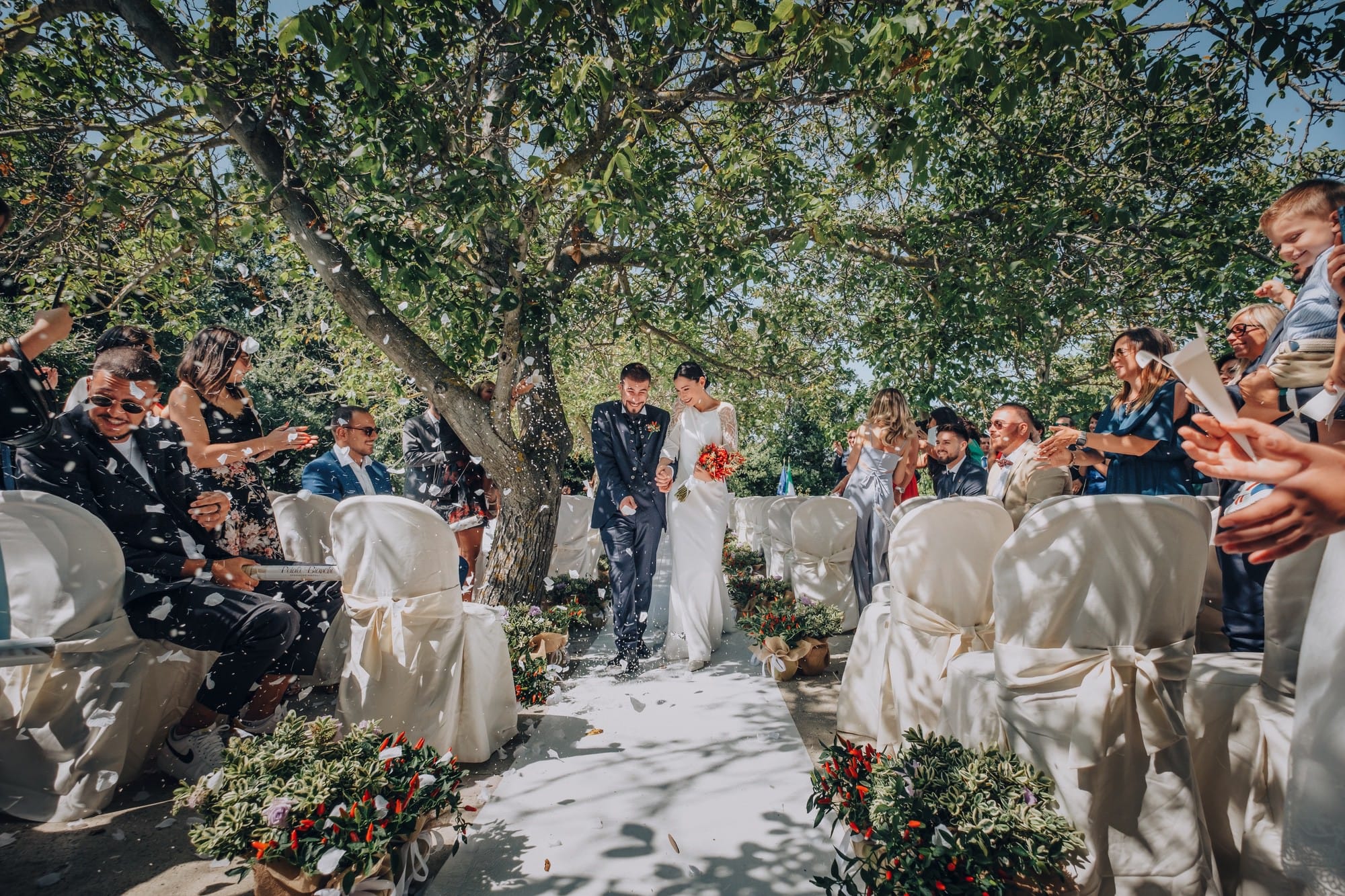 A civil ceremony in a tree-shaded garden, guests seated either side of the aisle, Pino Coduti Photography