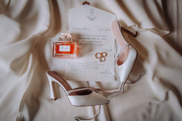 The invitation, perfume, rings and bridal shoes laid on silk, Pino Coduti Photography