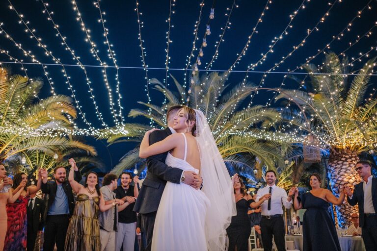 The couple dance under strings of lights, guests filming and cheering around them, Pino Coduti Photography