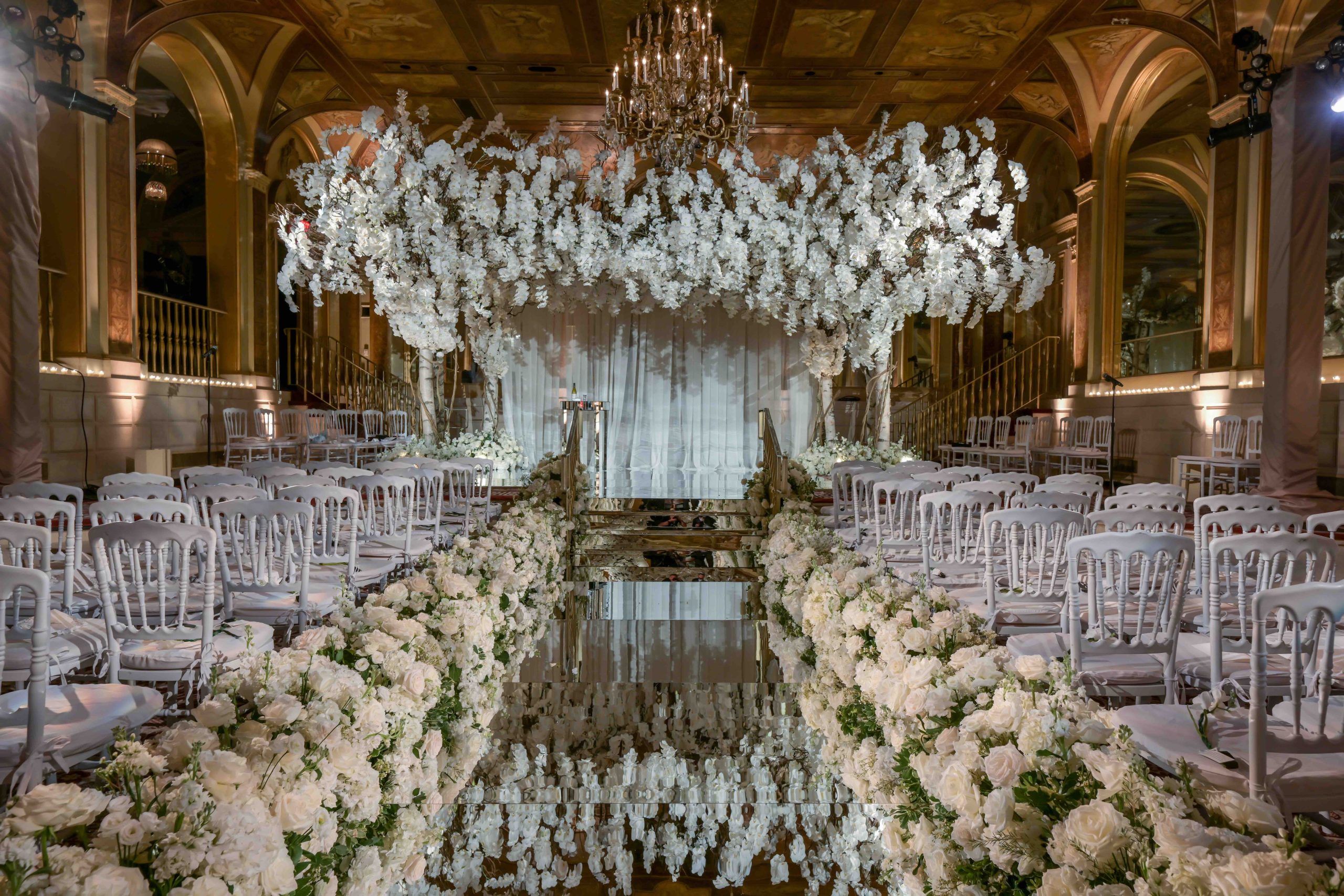 A ballroom ceremony at the Plaza Hotel, New York, with a floral chandelier above a mirrored aisle lined with white blooms, Preston Bailey