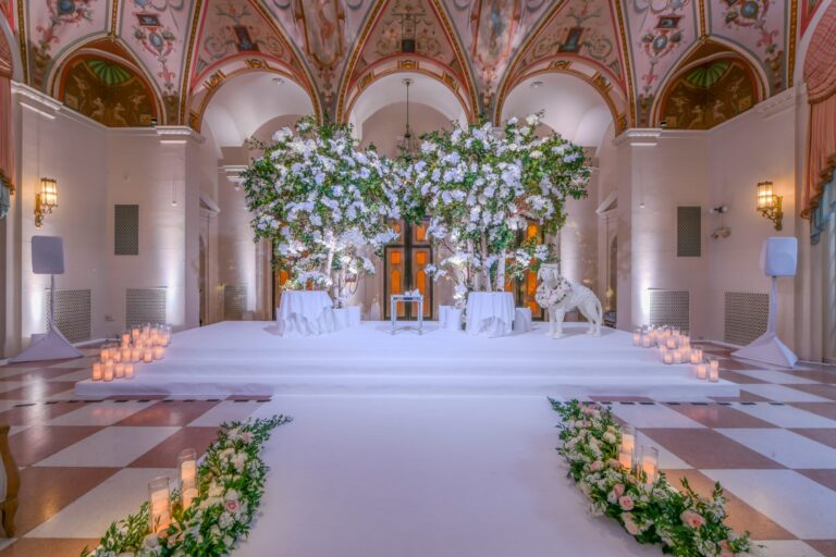A ceremony platform beneath two floral trees in a frescoed hall, with candles and flower-lined steps, Preston Bailey