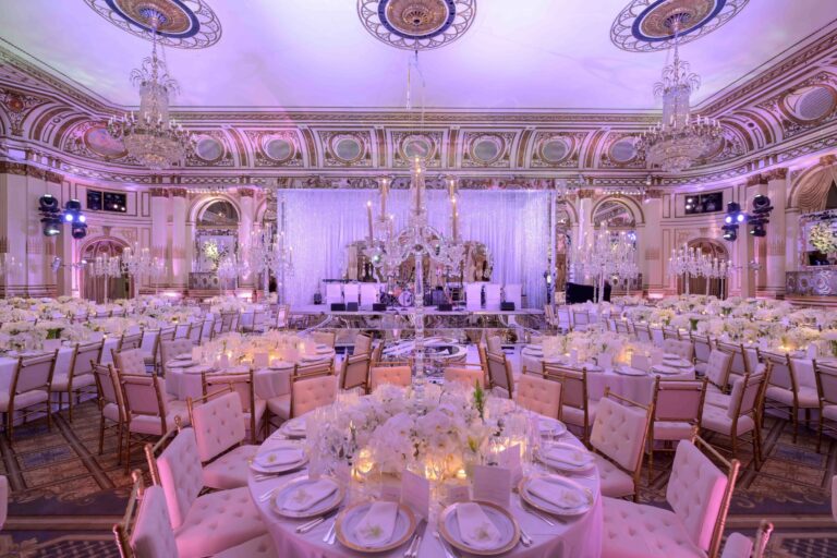 A ballroom reception in violet light at the Plaza Hotel, set with round tables and a stage, Preston Bailey
