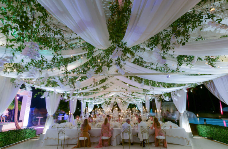A garden reception beneath white drapes and trailing greenery, beside a pool at dusk, Preston Bailey