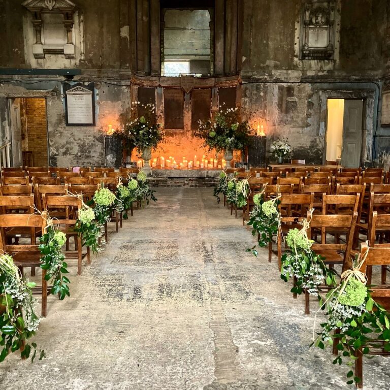 A candlelit aisle dressed with floral pew-ends, the Asylum Chapel, Peckham, Rebecca Mays