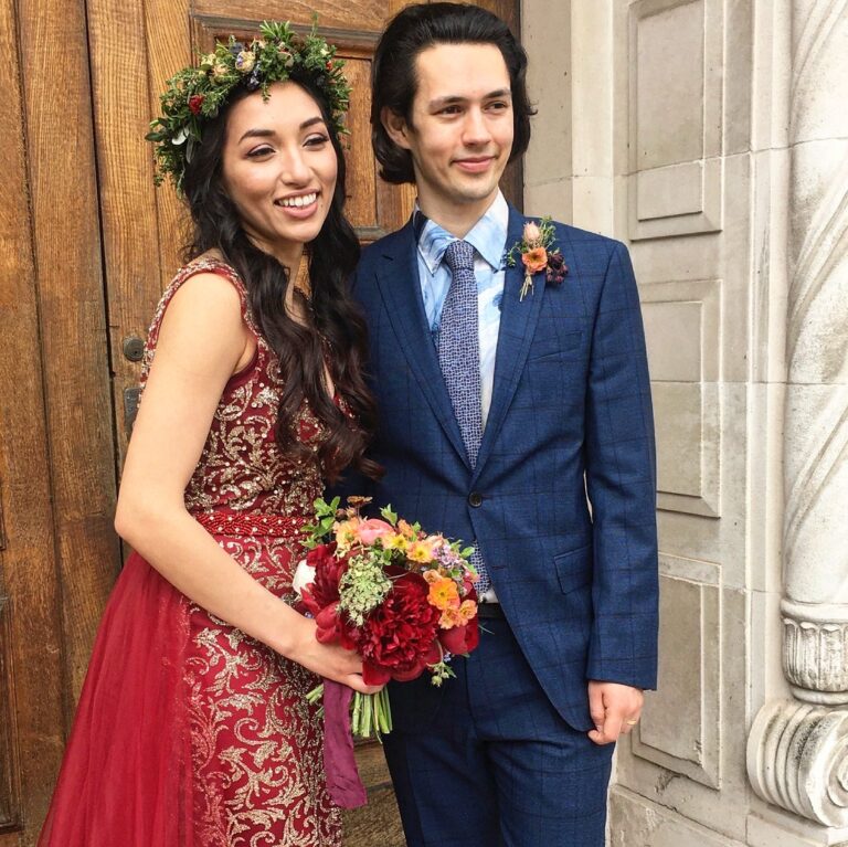 A bride in a red dress with a floral crown, and her groom, at the Asylum Chapel, Rebecca Mays