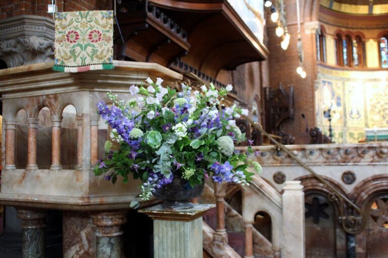 A pedestal arrangement of purple and white, inside an ornate church, Rebecca Mays