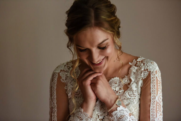 Bride smiling down at her hands in lace sleeves, Reflexion Studio