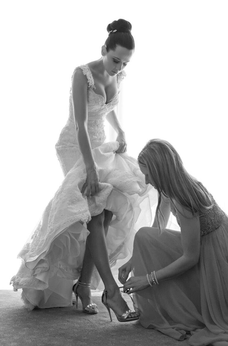 Bridesmaid helping the bride with her shoes, Reflexion Studio