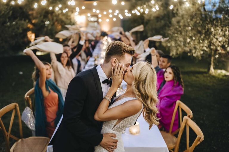 A kiss beside the dinner tables while guests cheer and wave napkins, at a private villa near Siena, Rellini Art Studio