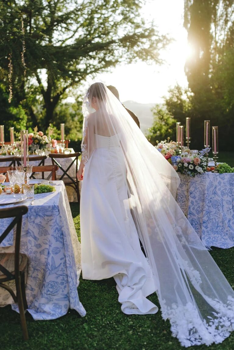 A bride in a long veil beside the dinner tables in the late sun, Borgo Laticastelli, Tuscany, Rellini Art Studio