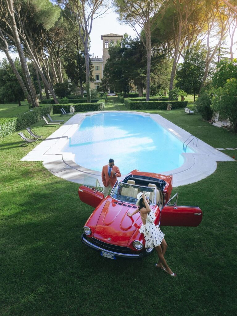 Guests by the pool and a vintage red car at a wedding party at La Torre di Pila, Perugia, Rellini Art Studio