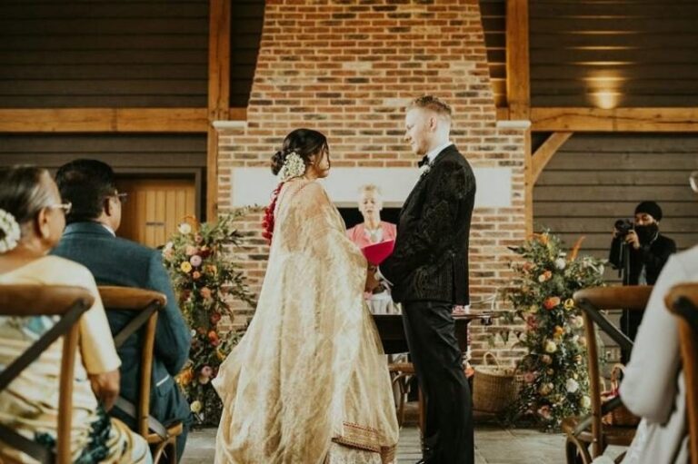 An indoor ceremony in the Great Barn, the couple exchanging vows against the exposed brick and oak frame, Retreat East