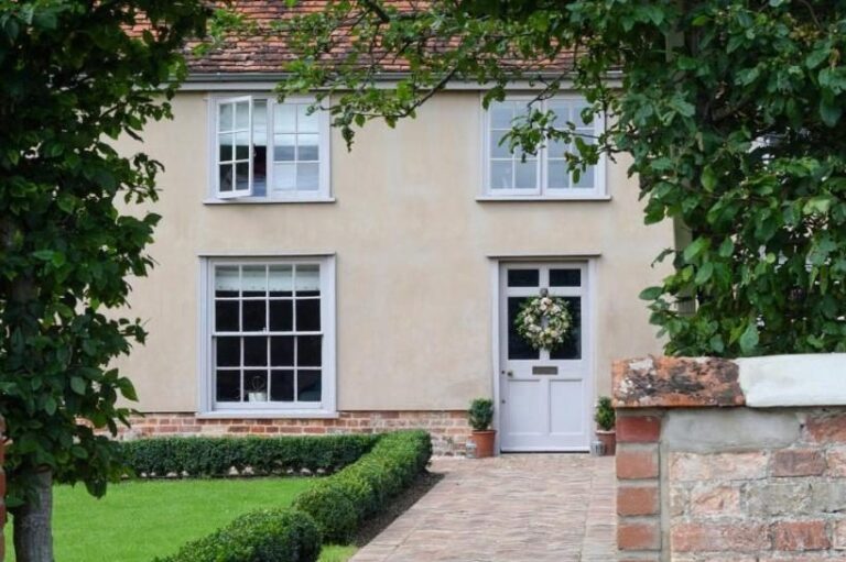 A restored farmhouse exterior with a lush greenery arch over the door, Retreat East