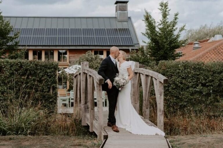 A couple on the rustic wooden garden bridge, the solar-roofed restaurant and spa building behind, Retreat East