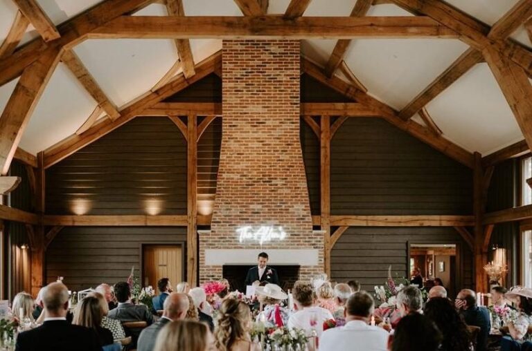 The Great Barn set for the reception, oak roof trusses and brick chimney above the top table, Retreat East