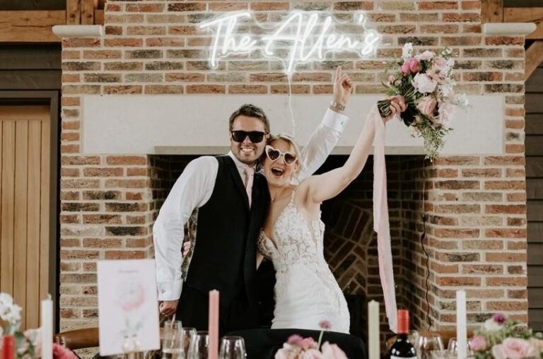 Newlyweds celebrating by the barn's brick fireplace beneath a floral display, Retreat East