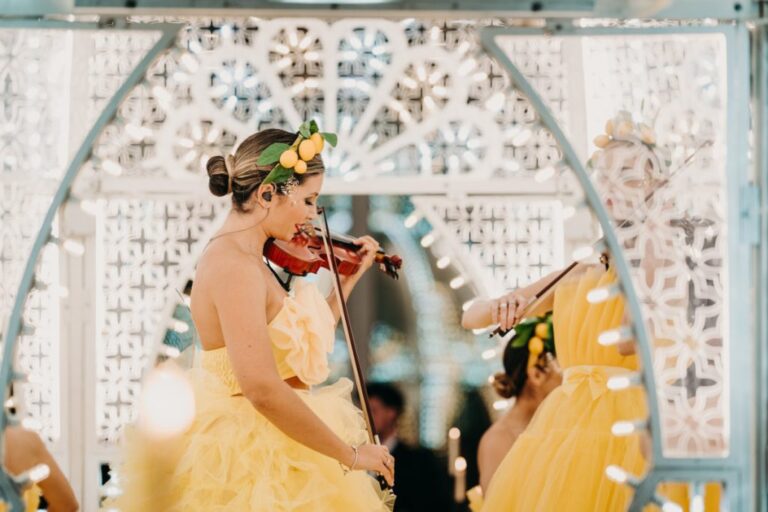 Violinists in yellow gowns on a stage framed with lights, Rinaldi Production