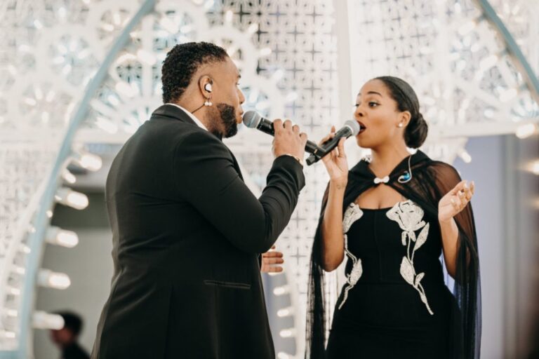 Vocal duet in front of an ornate white illuminated arch, Rinaldi Production