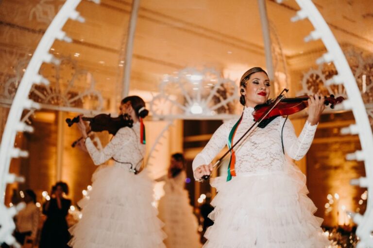 String players in white gowns performing in an amber-lit room, Rinaldi Production