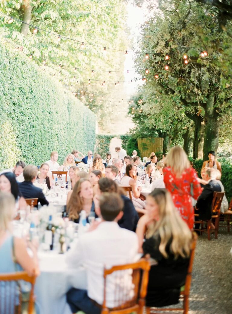 Guests at long tables beneath string lights and a tall hedge, Villa Il Poggiale, Rocco Daniele Photography