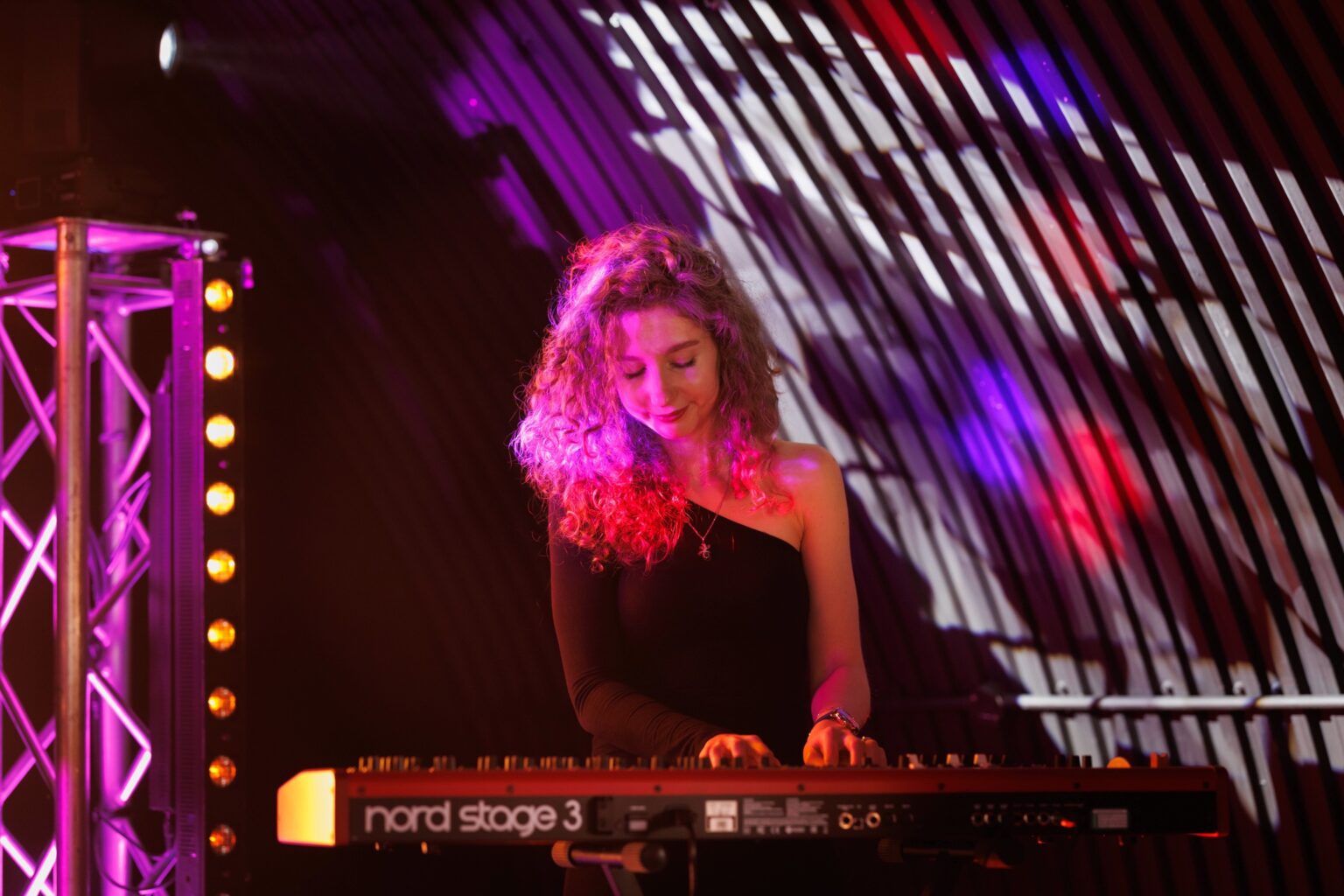 The keyboard player at a Nord Stage keyboard under pink and white stage lights