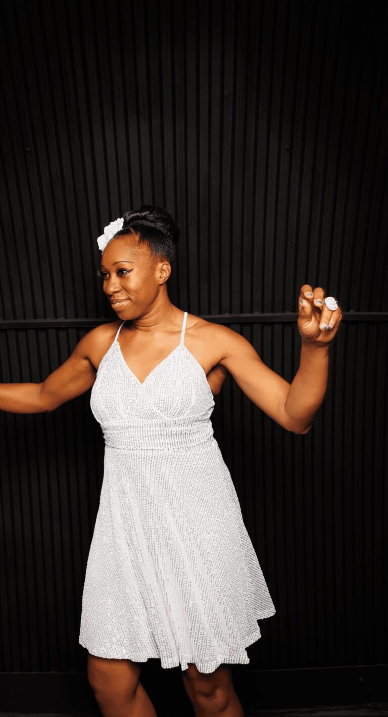 A vocalist dancing in a white halter dress against a black backdrop, Rocks The Room