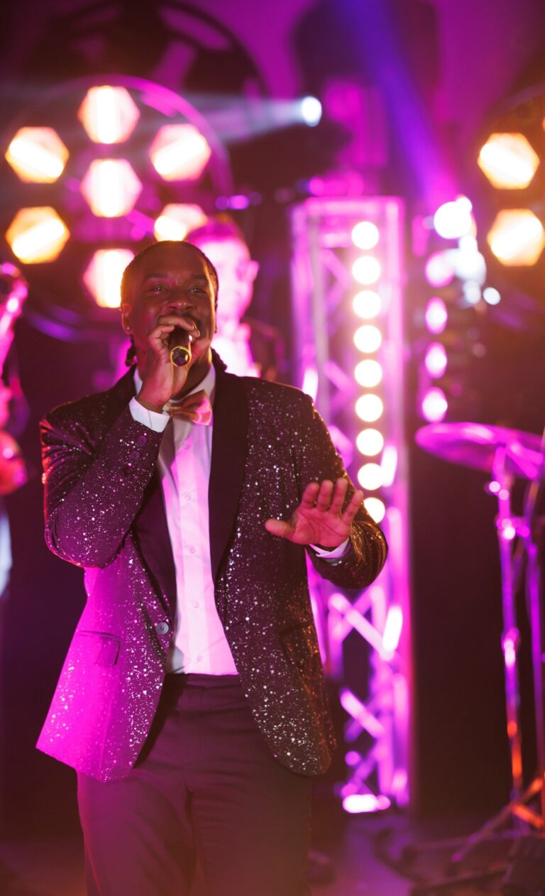 A male vocalist singing in front of stage lighting trusses, Rocks The Room