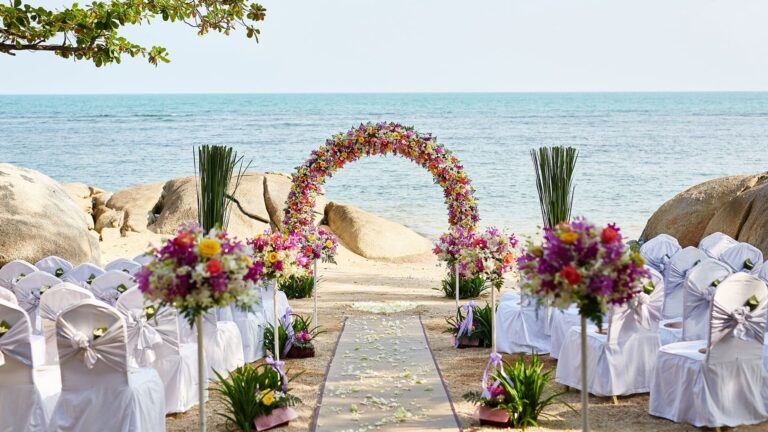 A flower arch and white chairs set out for a beach ceremony among the rocks, Rocky’s Boutique Resort