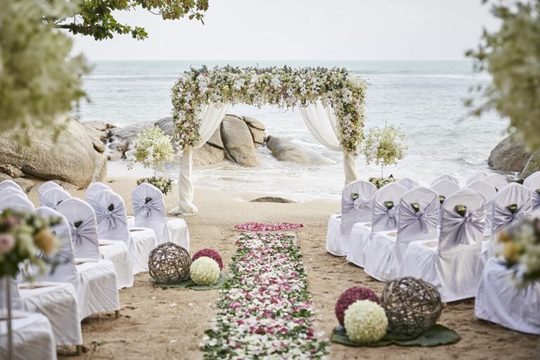 White chairs and a petal-strewn aisle leading to a floral arch on the beach, Rocky’s Boutique Resort