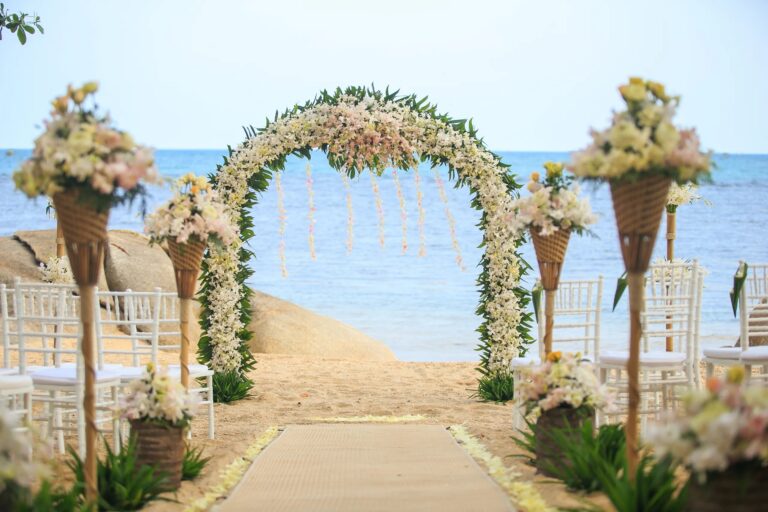 A floral arch framing the sea at the end of a beach aisle, Rocky’s Boutique Resort