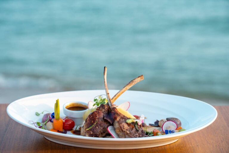 Lamb rack served on a white plate beside the sea, Rocky’s Boutique Resort