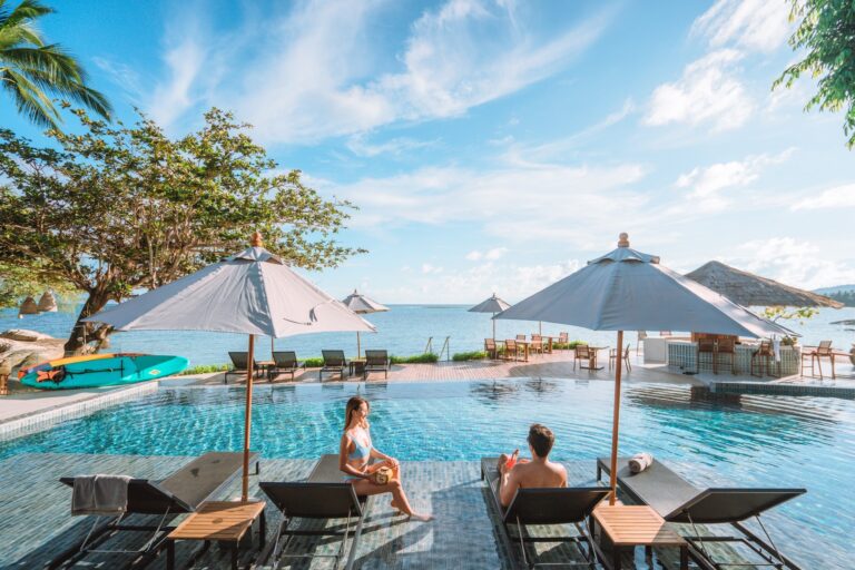 Guests on sun loungers beside the pool with the sea beyond, Rocky’s Boutique Resort