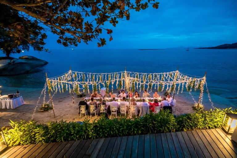 A wedding dinner on the beach under garlands of lights at dusk, Rocky’s Boutique Resort