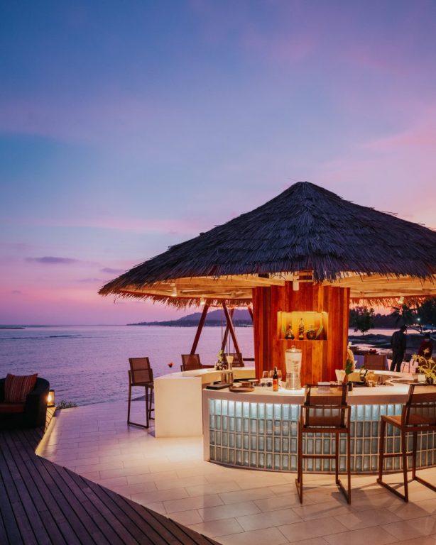 A thatched beach bar lit at dusk beside the water