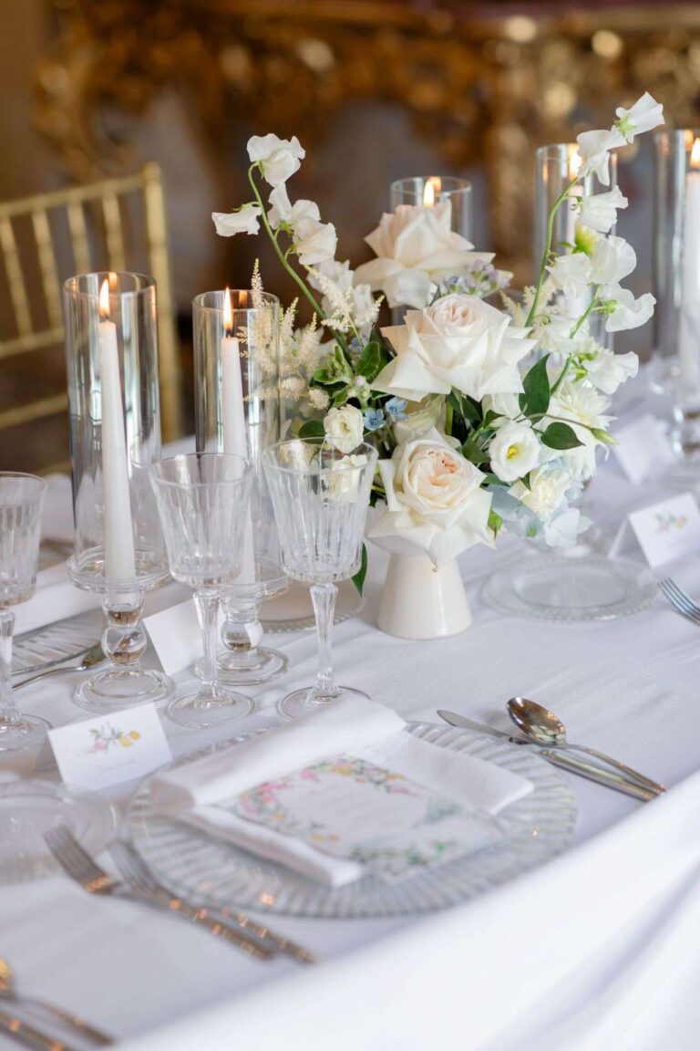 Table in white and gold with white flowers and tall candles under a chandelier (Ashley & Sergio; venue not named on the site), RoRas Destination Wedding