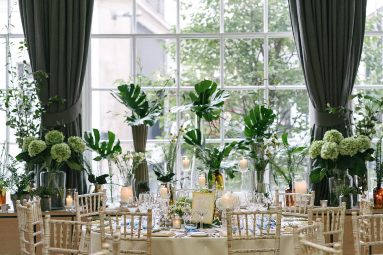 Round tables set before tall windows hung with foliage, RSA House