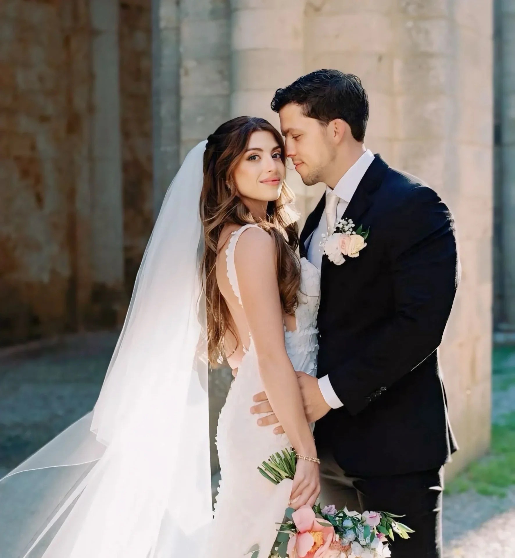 Couple embracing in a stone cloister, bridal hair and veil styled on location, Samantha Pretto