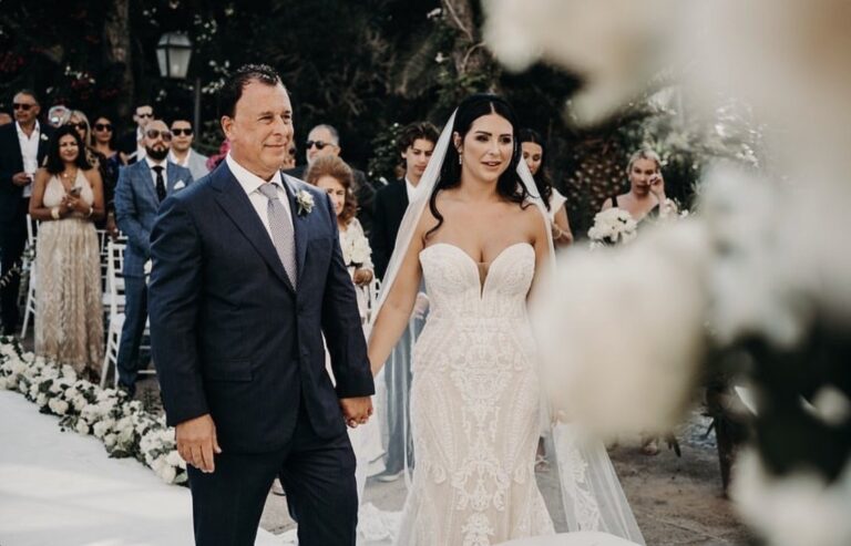 Bride on her father's arm walking the aisle between white flowers, Samantha Pretto
