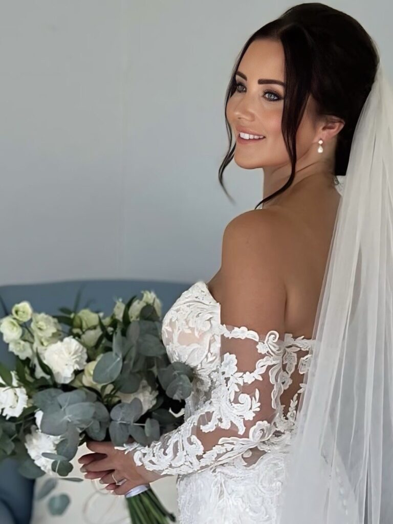 Bride with a loose low chignon and long veil, holding a white bouquet, Samantha Pretto