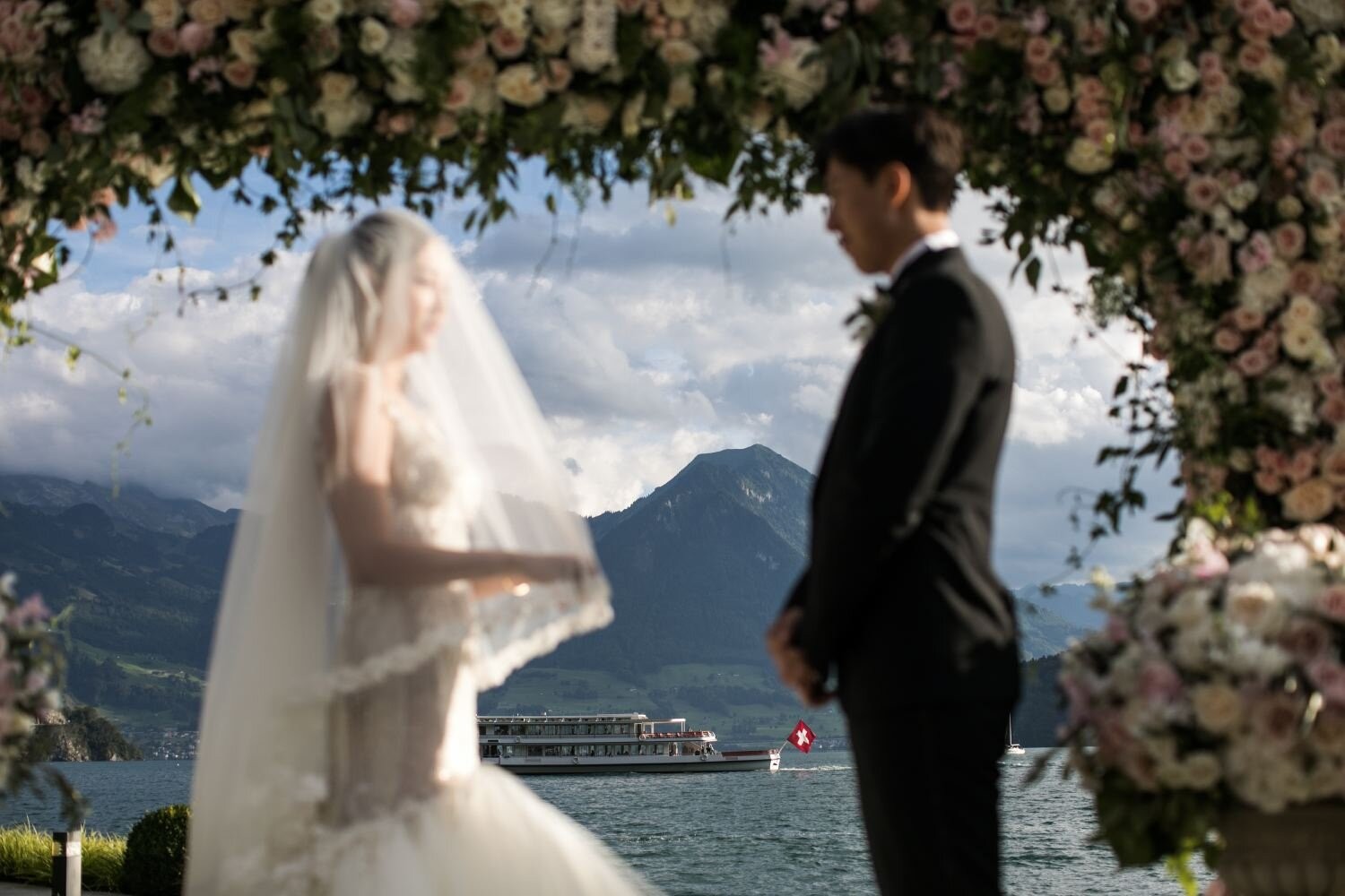 Bride and groom beneath a floral arch with a lake and mountains behind, Samuel Lippke Studios