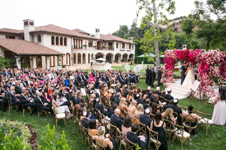 Guests seated for a garden ceremony before a pink floral arch, villa behind, Samuel Lippke Studios