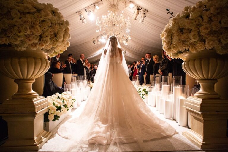 Bride with a long veil at the end of an aisle flanked by white floral urns, Samuel Lippke Studios