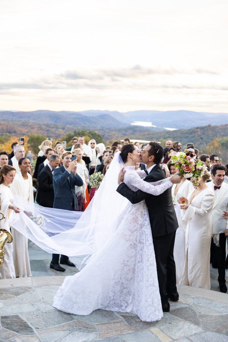 Couple embracing with a long veil on a hilltop terrace, guests around them, Samuel Lippke Studios
